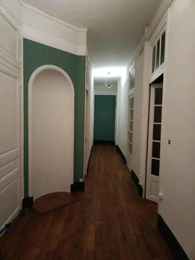 Même couloir après rénovation : parquet en chêne foncé, arche peinte en vert profond, corniches et portes vitrées repeintes en blanc