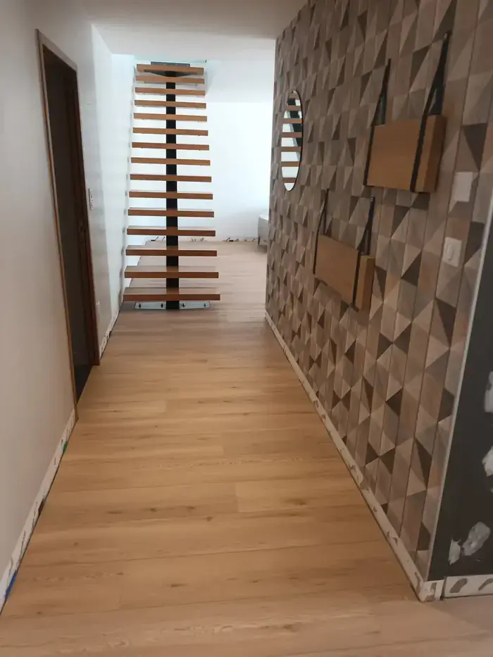 Même entrée terminée : parquet en chêne clair, mur habillé d'un papier peint géométrique en relief, escalier à marches bois