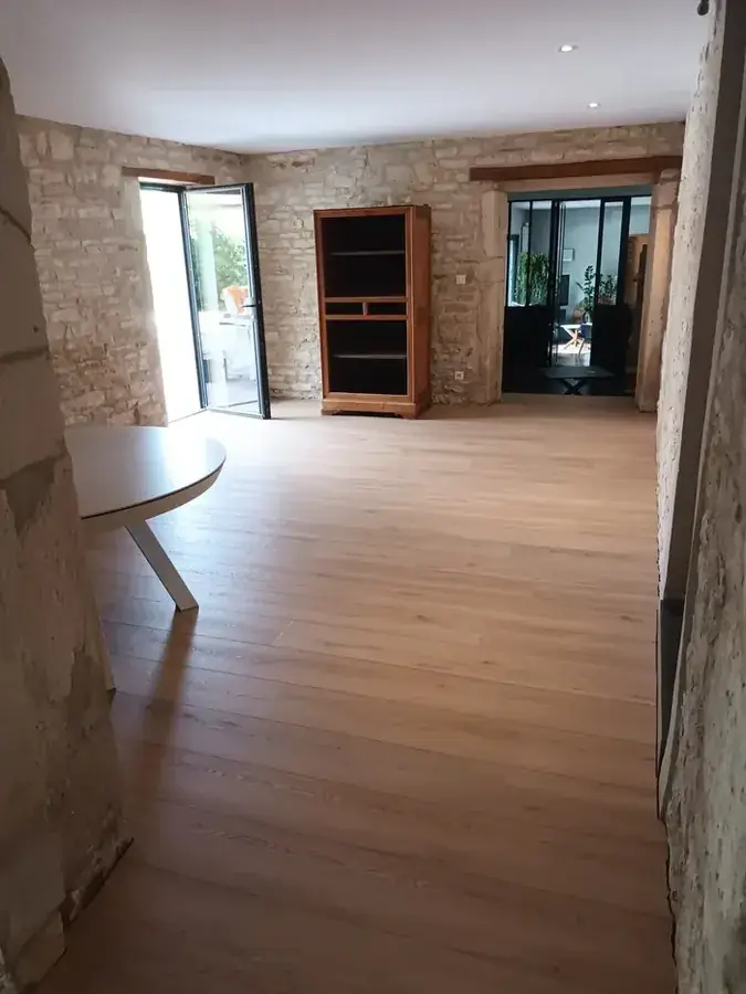 Même séjour après rénovation : murs en pierre rejointoyée, parquet en chêne clair, plafond lisse et verrière noire