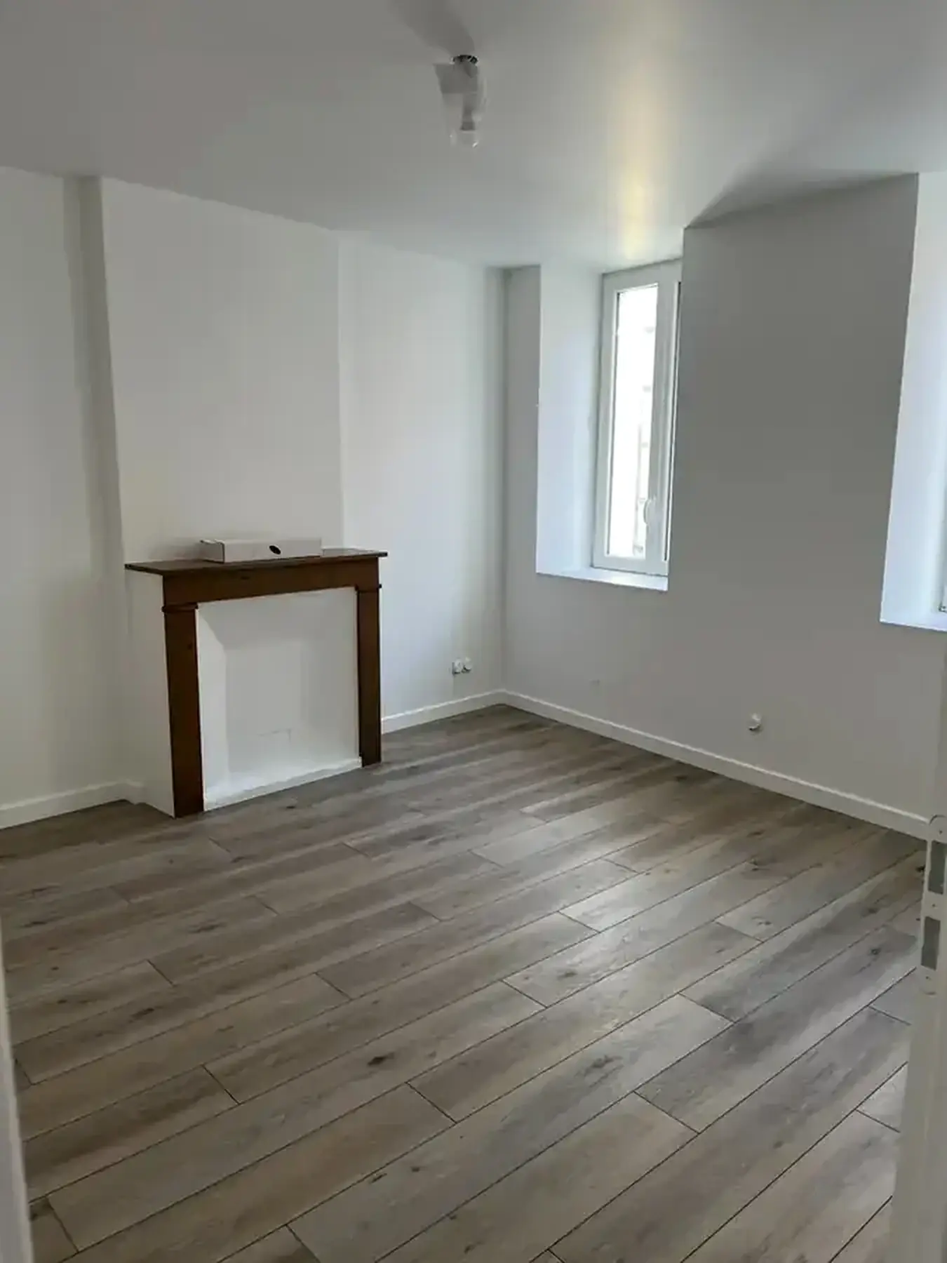 Même pièce terminée : murs et plafond blancs, sol stratifié bois gris, cheminée ancienne conservée et repeinte
