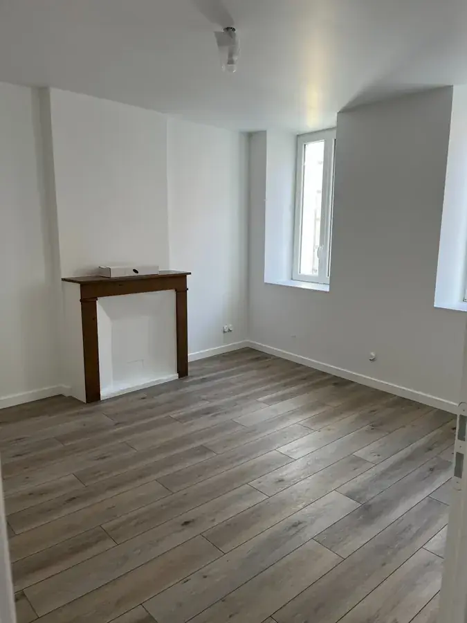 Pi&egrave;ce r&eacute;nov&eacute;e&nbsp;: murs blancs, sol stratifi&eacute; gris et manteau de chemin&eacute;e en bois conserv&eacute;