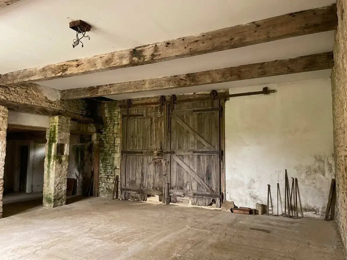 Int&eacute;rieur avant travaux&nbsp;: murs en pierre pi&eacute;quet&eacute;s d'humidit&eacute;, poutres anciennes et portes de grange en bois