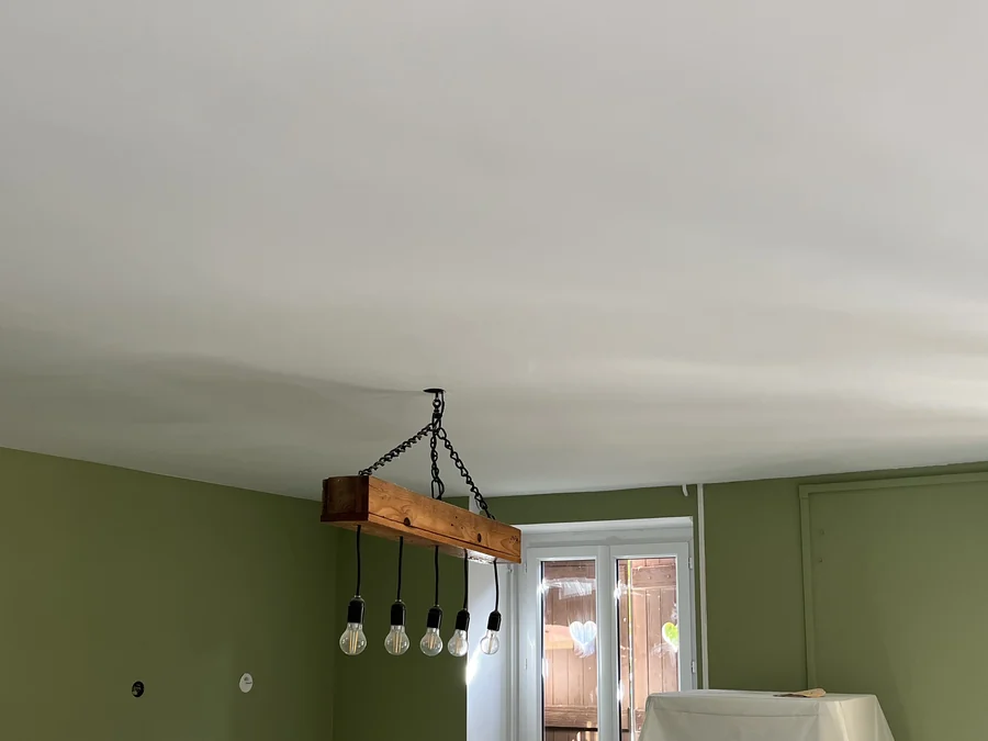 Même pièce terminée : plafond blanc continu, murs vert sauge, et la même poutre à cinq ampoules suspendue au plafond