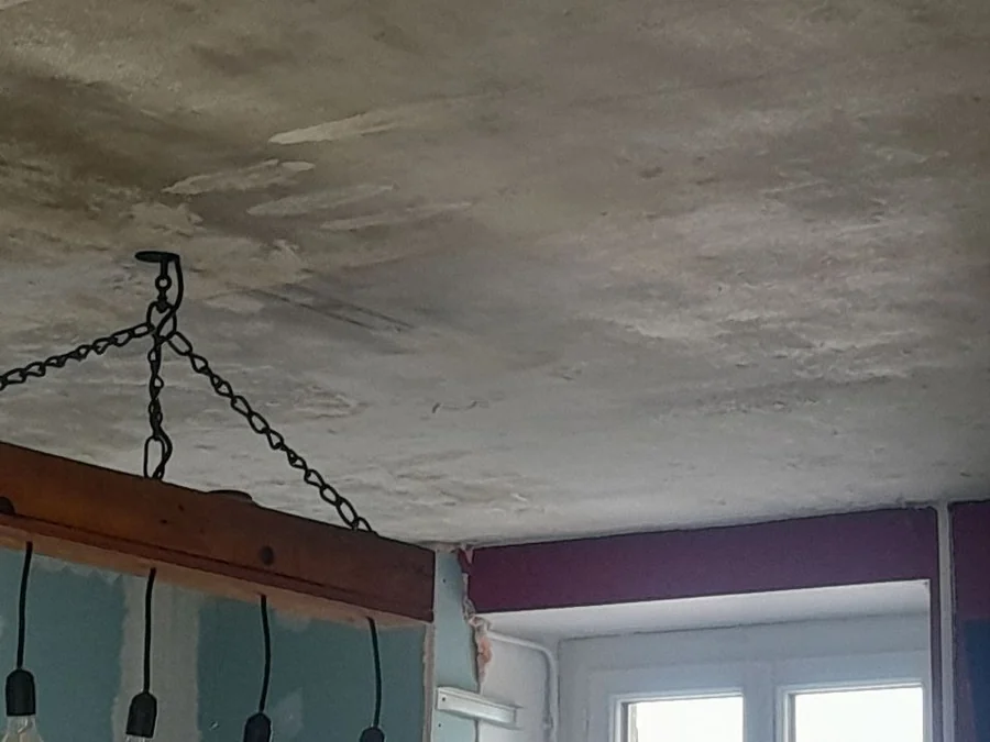 Plafond ancien décroûté, marbré de gris et de beige, sous une poutre suspendue par des chaînes portant cinq ampoules